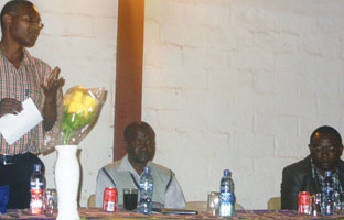 Zambian branch chairman, Rodgers Kayombo, speaks at the launch. Vice chairman Widdy Chimba is in the middle and guest of honour, Mwendapole Muleng, on the right